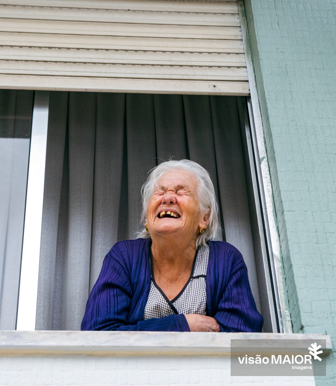 Mulher de cabelo branco a rir de olhos fechados à janela