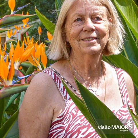 Mulher de cabelo e olhos claros, no meio de flores, com vestido de mangas à cava