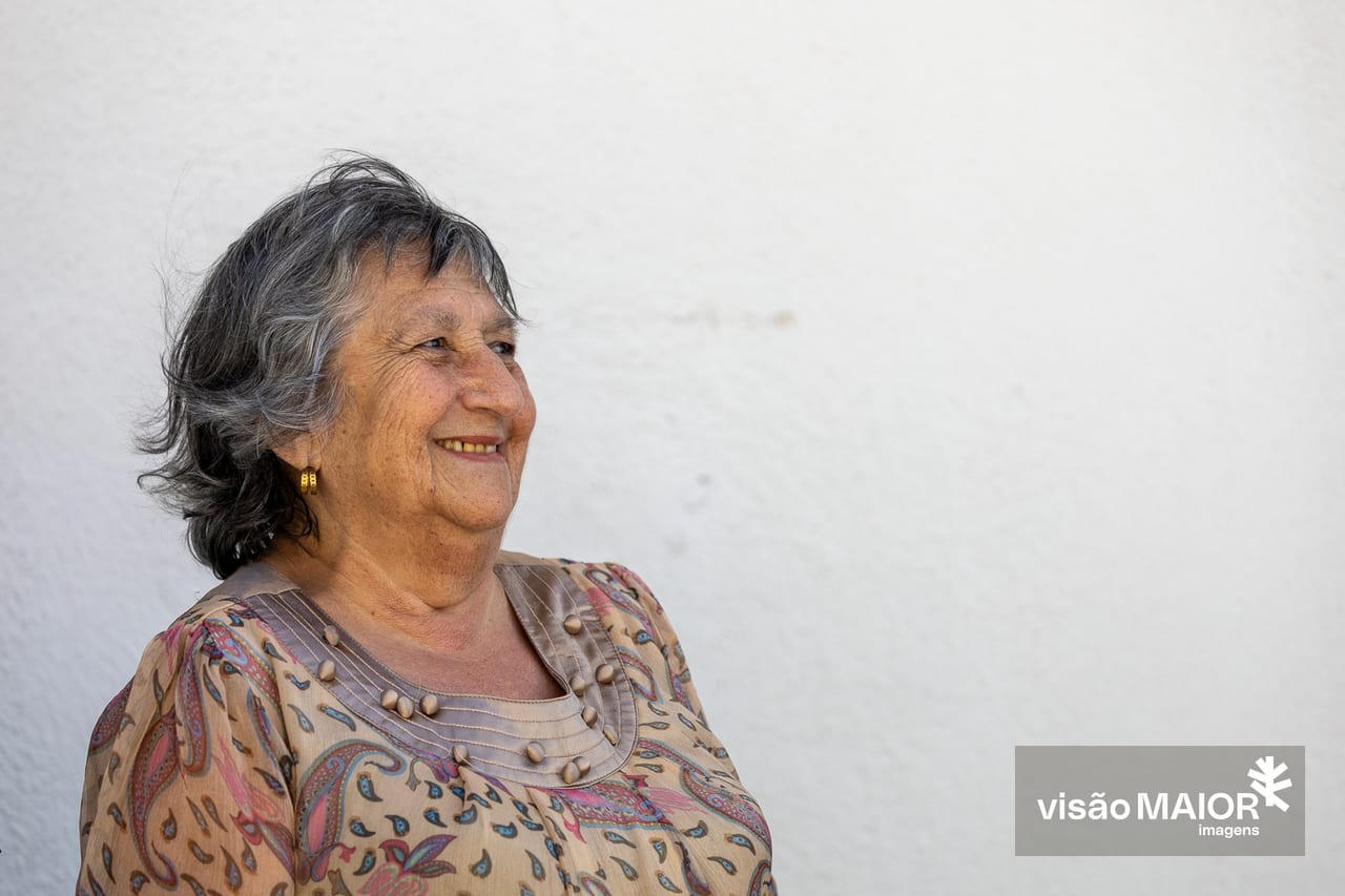 Mulher sorridente de cabelo grisalho e brincos de lado a sorrir