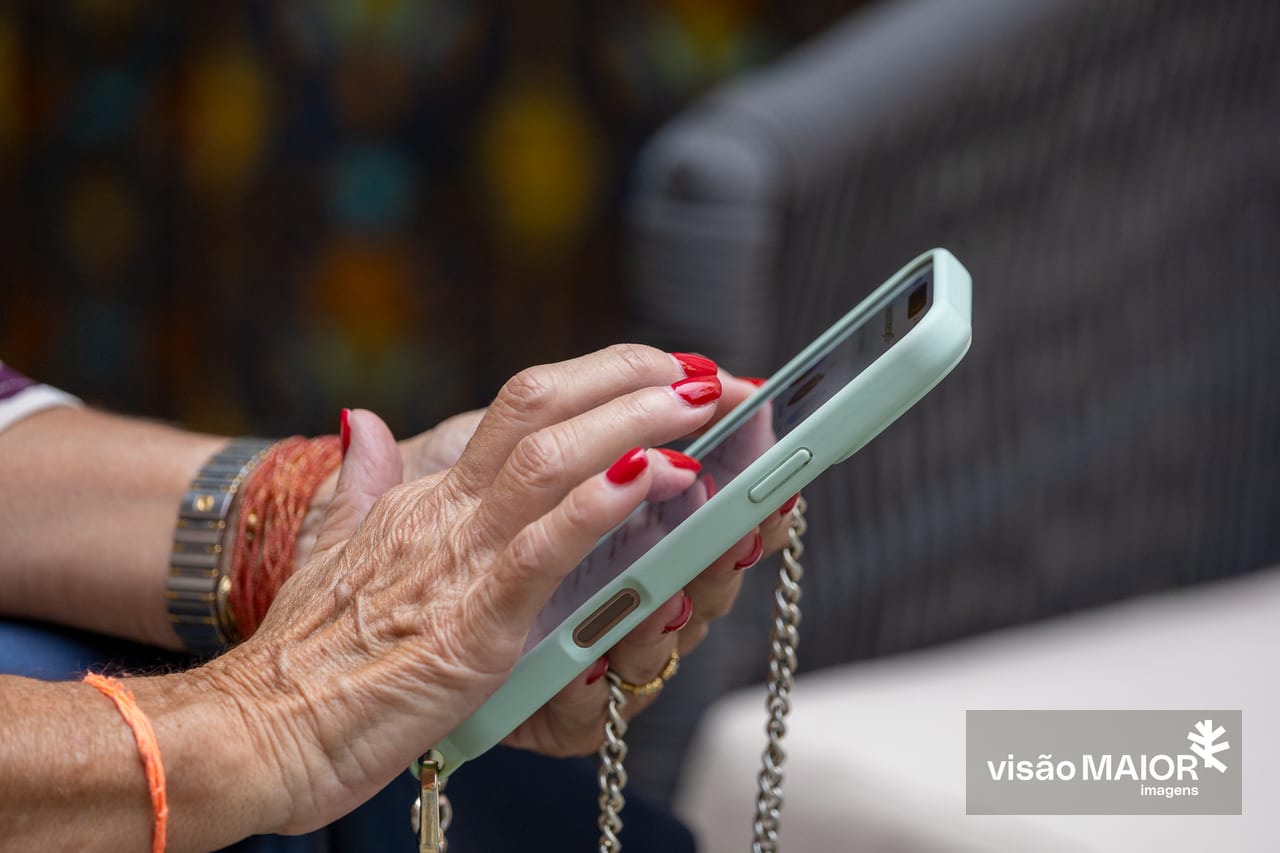 Mão de mulher com unhas pintadas e pulseiras a pegar num telemóvel com alça de corrente